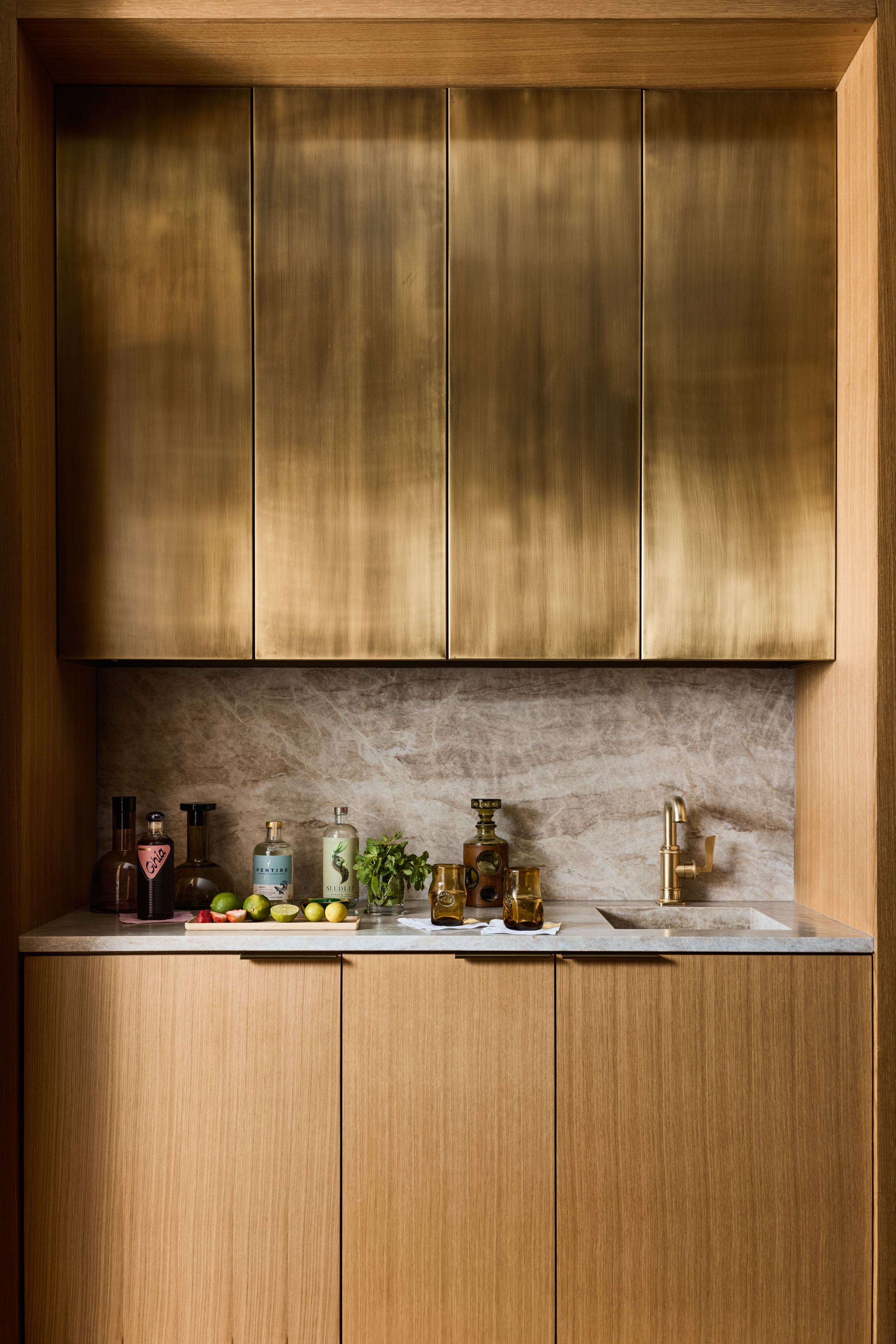 Oak wet bar with aged brass cabinetry and natural stone